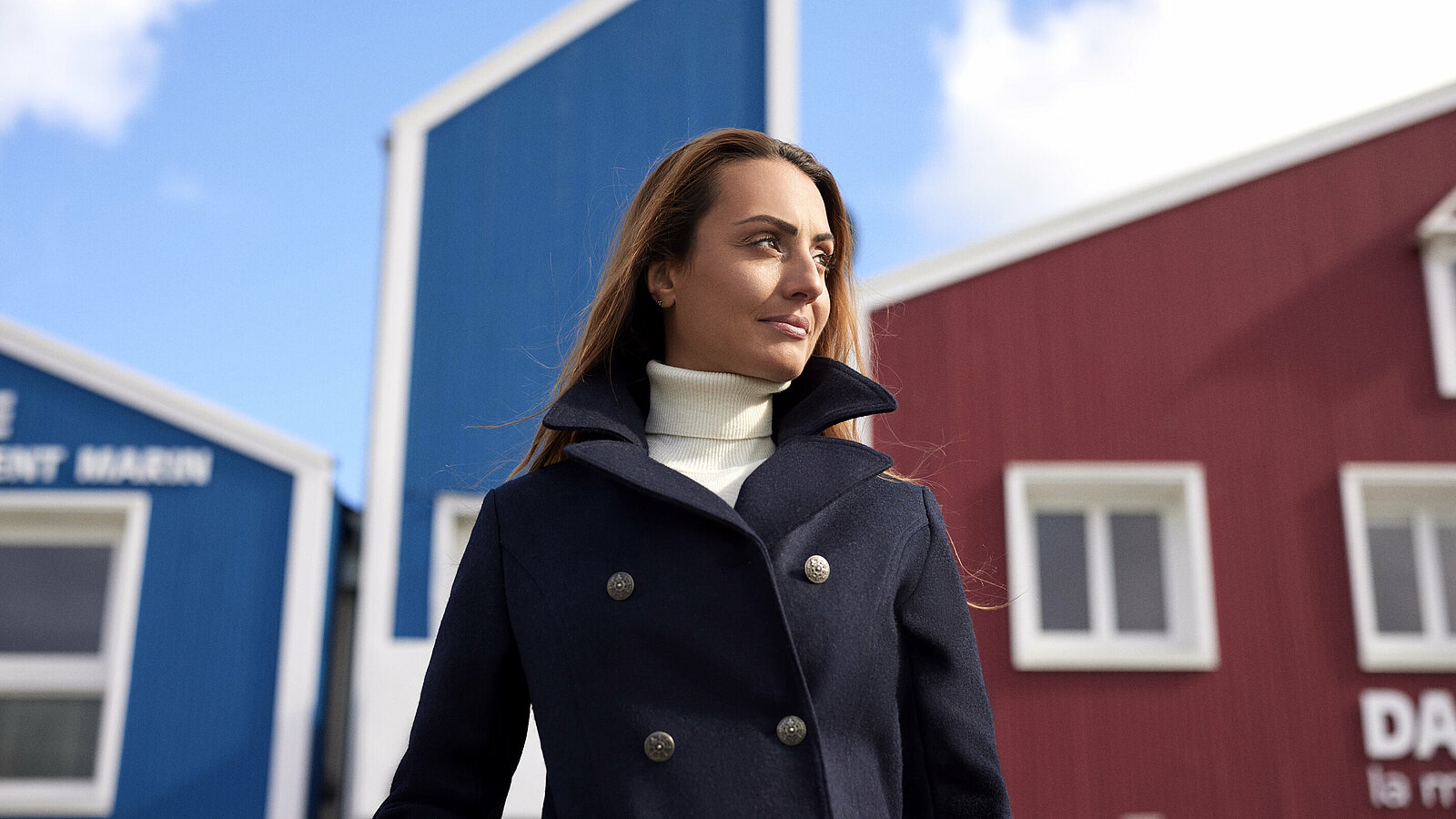 Femme devant le bâtiment bleu et rouge de Dalmard Marine sur le port de Paimpol en caban